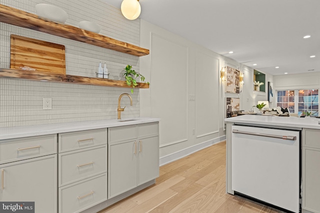 kitchen with white dishwasher, light hardwood / wood-style floors, sink, and decorative backsplash