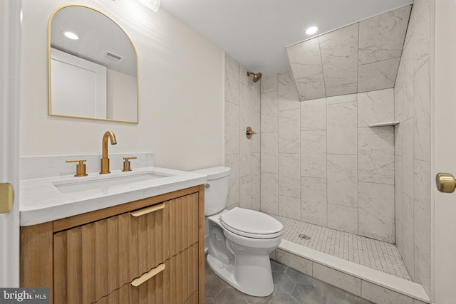 bathroom with tile patterned flooring, vanity, a tile shower, and toilet