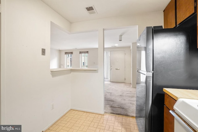 kitchen with light countertops, brown cabinetry, visible vents, and freestanding refrigerator