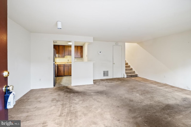 unfurnished living room featuring stairs, light colored carpet, visible vents, and a sink