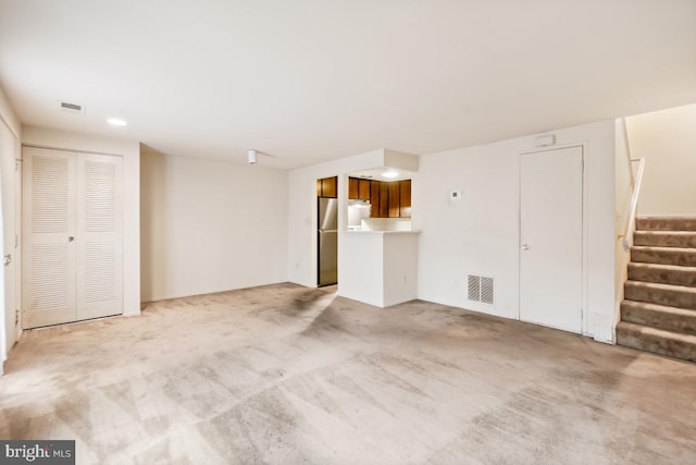 unfurnished living room with visible vents, light carpet, and stairs