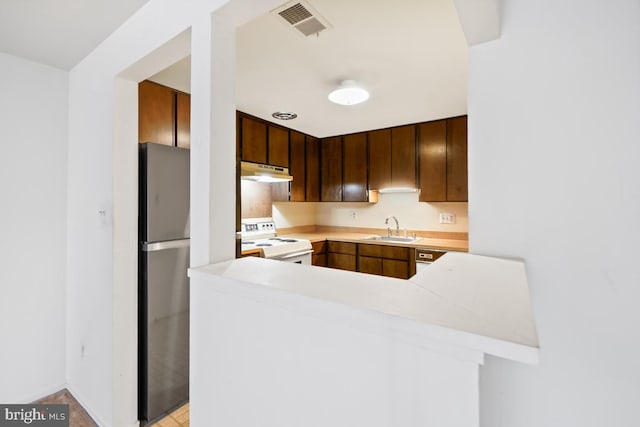 kitchen featuring electric stove, under cabinet range hood, a sink, freestanding refrigerator, and light countertops