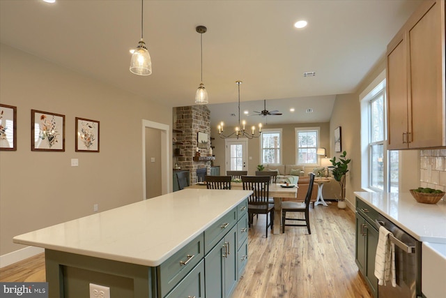 kitchen with a stone fireplace, hanging light fixtures, light hardwood / wood-style flooring, stainless steel dishwasher, and a kitchen island