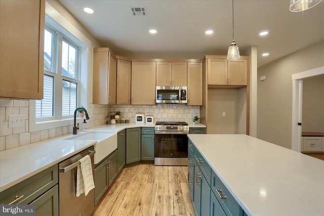 kitchen featuring sink, appliances with stainless steel finishes, tasteful backsplash, light hardwood / wood-style floors, and decorative light fixtures