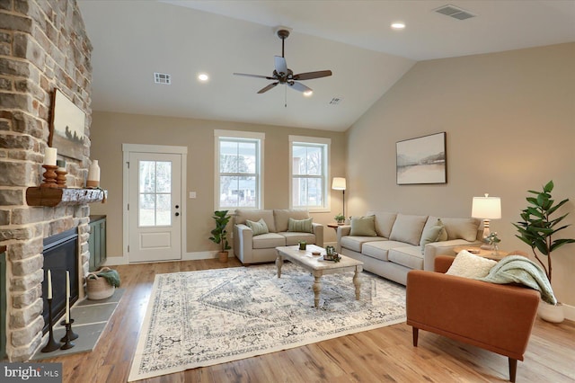 living room with lofted ceiling, a stone fireplace, light hardwood / wood-style floors, and ceiling fan