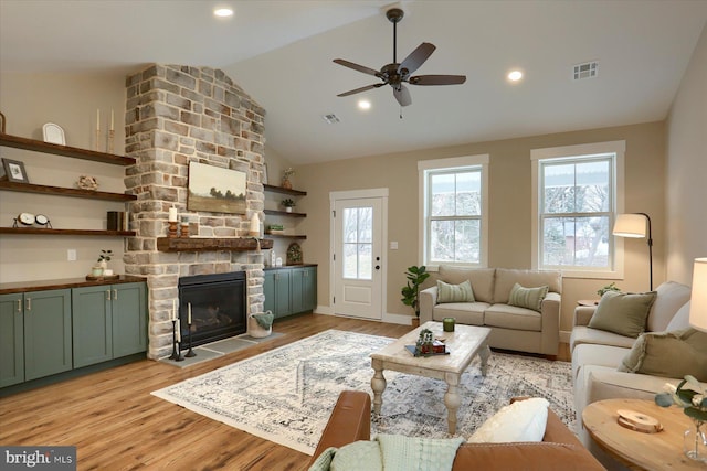 living room featuring a stone fireplace, a healthy amount of sunlight, and light hardwood / wood-style flooring