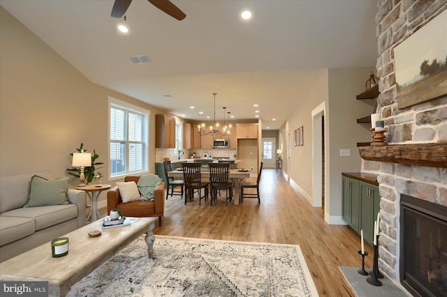 living room with a stone fireplace, sink, ceiling fan with notable chandelier, and light wood-type flooring