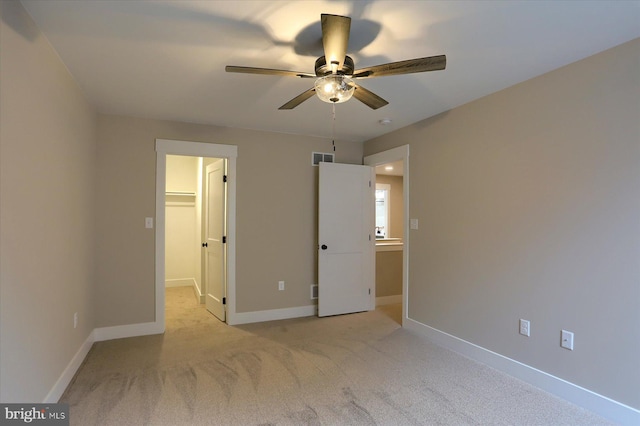 unfurnished bedroom with ceiling fan, a walk in closet, and light carpet