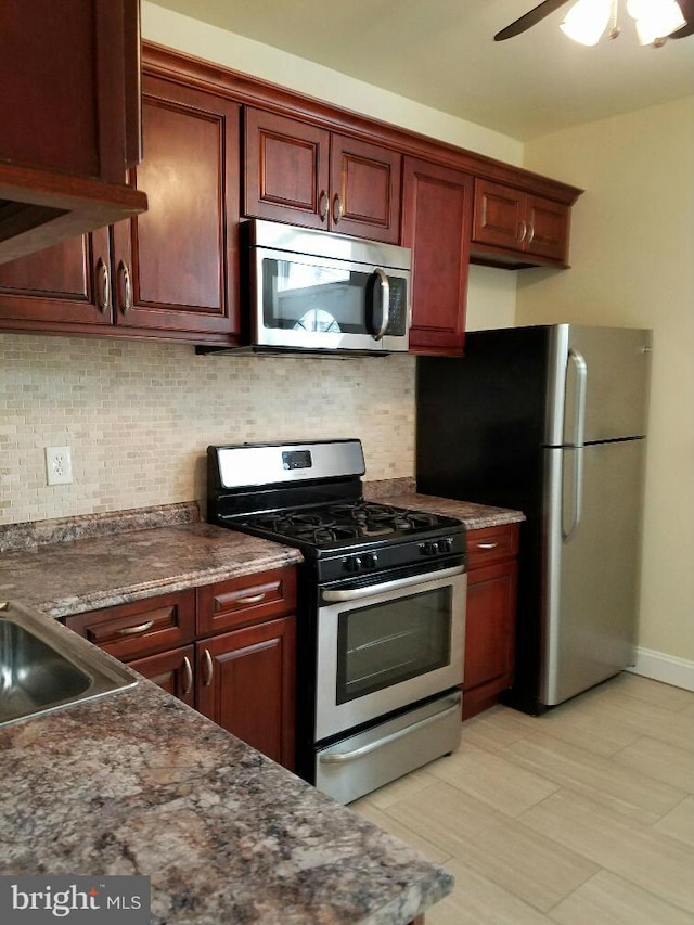 kitchen with dark stone countertops, ceiling fan, stainless steel appliances, and backsplash