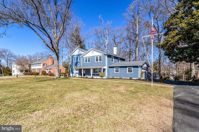 view of front of property featuring covered porch, a chimney, aphalt driveway, and a front yard