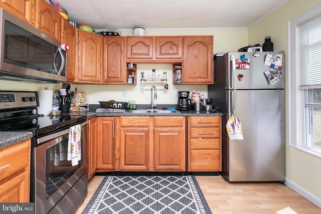 kitchen featuring sink, light hardwood / wood-style flooring, ornamental molding, appliances with stainless steel finishes, and dark stone counters