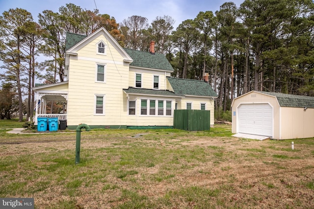 rear view of property with a garage, an outdoor structure, and a yard