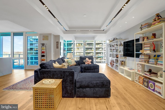 living room featuring light wood-style flooring, floor to ceiling windows, and a raised ceiling