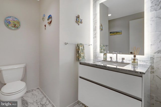 bathroom featuring toilet, marble finish floor, vanity, and baseboards