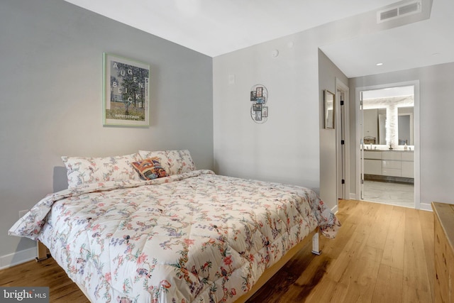 bedroom with baseboards, visible vents, connected bathroom, and hardwood / wood-style floors