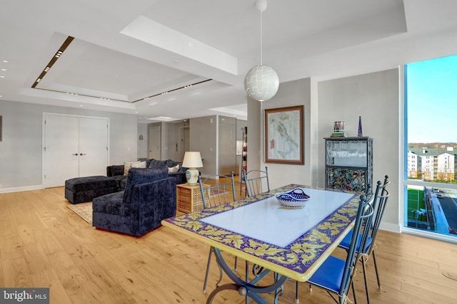 dining room featuring light wood-style floors, baseboards, and a raised ceiling