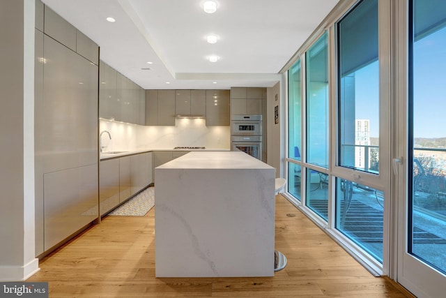 kitchen featuring stainless steel double oven, a sink, a kitchen island, gray cabinets, and modern cabinets