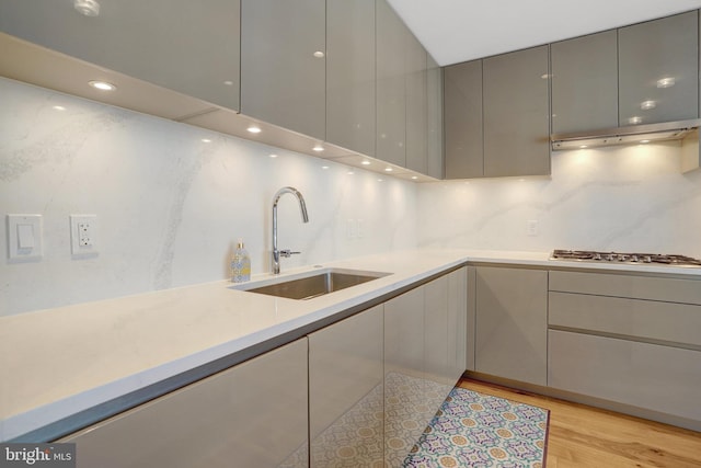 kitchen featuring under cabinet range hood, stainless steel gas cooktop, a sink, light countertops, and gray cabinets