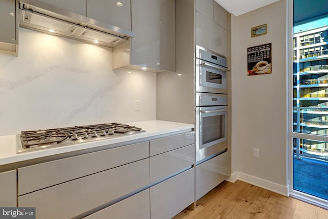 kitchen with light wood-style floors, light countertops, ventilation hood, appliances with stainless steel finishes, and modern cabinets