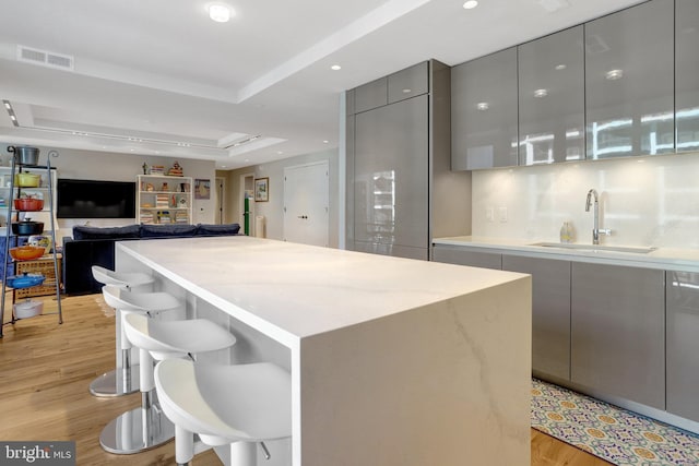 kitchen featuring a breakfast bar area, visible vents, gray cabinetry, a sink, and modern cabinets