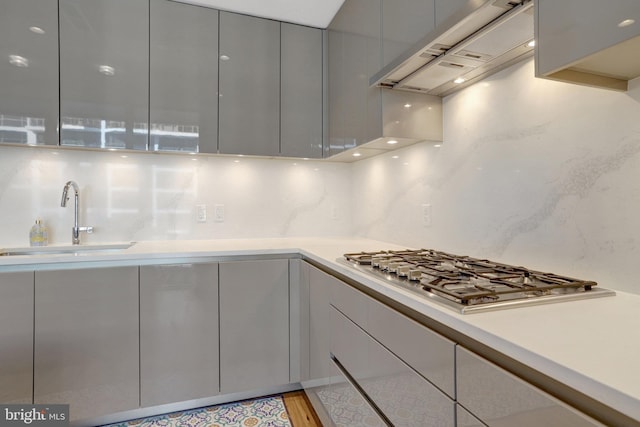 kitchen with a sink, light countertops, premium range hood, stainless steel gas cooktop, and backsplash