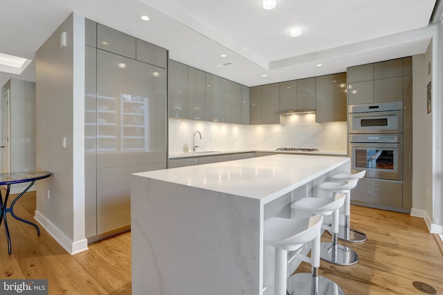 kitchen with light countertops, gray cabinetry, a sink, modern cabinets, and a kitchen bar