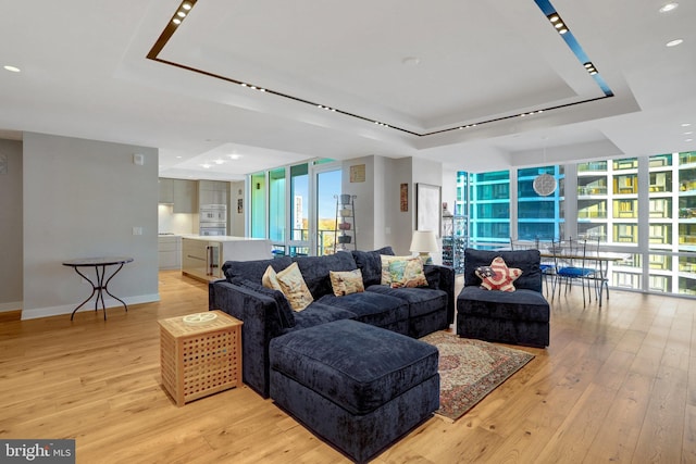 living area featuring baseboards, a tray ceiling, light wood-style floors, and floor to ceiling windows