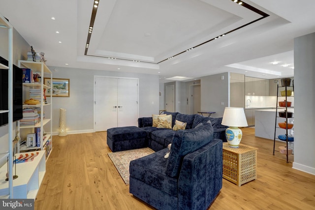 living area with light wood-style flooring, a tray ceiling, and baseboards