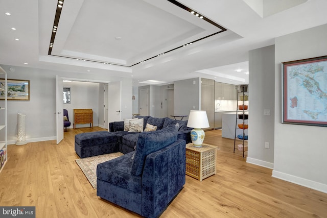 living room featuring a tray ceiling, light wood-type flooring, and baseboards