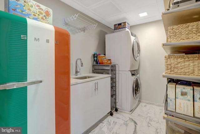 laundry room with stacked washer and dryer, cabinet space, baseboards, marble finish floor, and a sink