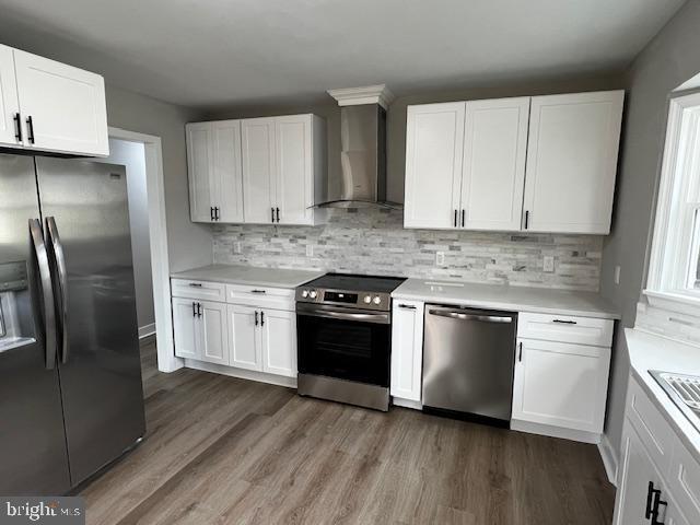 kitchen with wall chimney exhaust hood, stainless steel appliances, and white cabinets