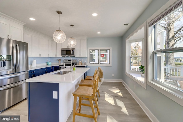 kitchen featuring blue cabinets, sink, appliances with stainless steel finishes, a kitchen island with sink, and white cabinets