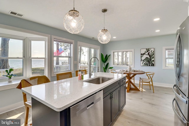 kitchen with pendant lighting, sink, appliances with stainless steel finishes, light stone counters, and an island with sink