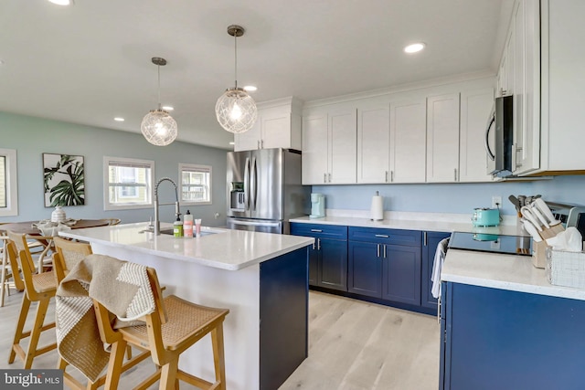 kitchen with appliances with stainless steel finishes, an island with sink, white cabinets, blue cabinets, and decorative light fixtures