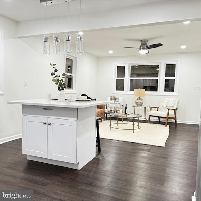 kitchen with dark wood-type flooring, a kitchen bar, white cabinetry, decorative light fixtures, and a center island