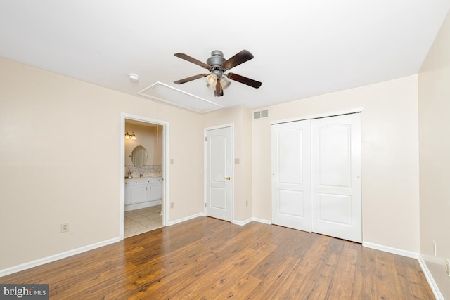 unfurnished bedroom featuring ceiling fan, ensuite bath, wood-type flooring, and a closet