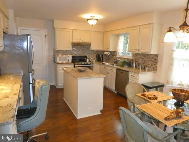 kitchen with a kitchen island, light stone countertops, stainless steel appliances, and decorative light fixtures