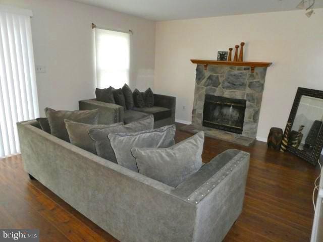 living room with dark hardwood / wood-style flooring and a stone fireplace