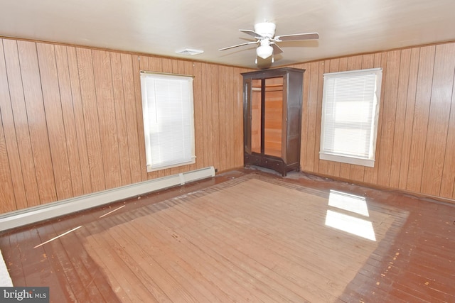 empty room featuring wood-type flooring, visible vents, baseboard heating, ceiling fan, and wooden walls