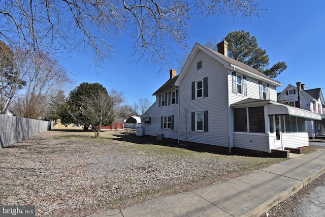 view of side of home featuring a sunroom, fence, and a chimney