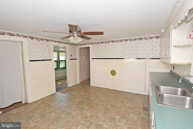 kitchen featuring wallpapered walls, wainscoting, dark countertops, white cabinetry, and a sink