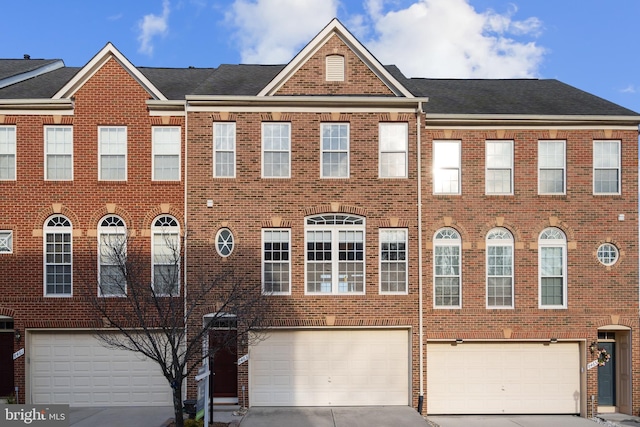 townhome / multi-family property with driveway, a shingled roof, a garage, and brick siding