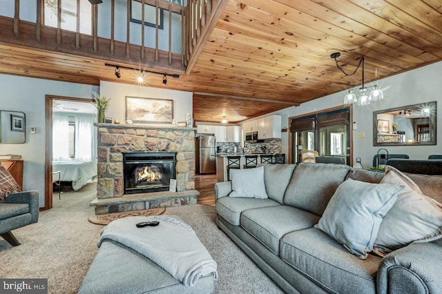 carpeted living room with wood ceiling, a stone fireplace, rail lighting, and a high ceiling