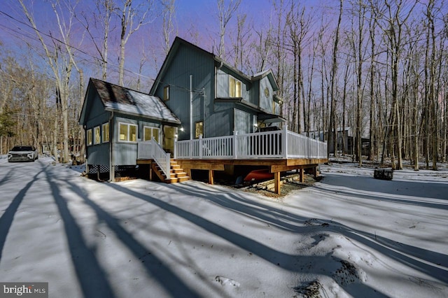 snow covered back of property featuring a wooden deck and a sunroom