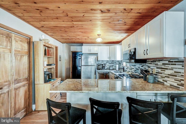 kitchen with white cabinetry, appliances with stainless steel finishes, kitchen peninsula, and light stone counters