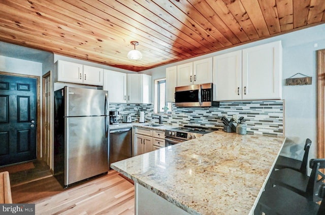 kitchen featuring white cabinetry, light stone counters, kitchen peninsula, stainless steel appliances, and decorative backsplash