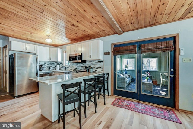 kitchen with stainless steel appliances, a kitchen breakfast bar, white cabinets, decorative backsplash, and kitchen peninsula