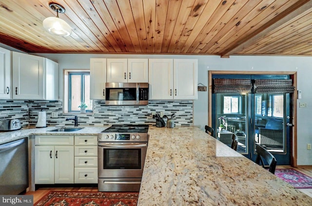 kitchen with light stone counters, decorative light fixtures, white cabinets, and appliances with stainless steel finishes