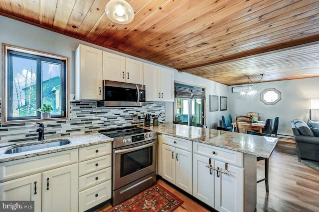 kitchen with a kitchen bar, sink, hanging light fixtures, appliances with stainless steel finishes, and kitchen peninsula