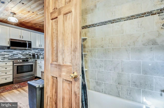 kitchen with white cabinetry, wood ceiling, stainless steel appliances, light hardwood / wood-style floors, and backsplash